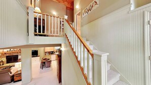 A multi-level home interior with a wooden staircase, a kitchen area, and a living space with a fireplace. - Acorn Cottage by Taylor Made Deep Creek (Oakland)