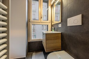 A modern bathroom with a wooden vanity, a large mirror, and a window with a grid pattern. - Monolocale - Darsena (Milano)
