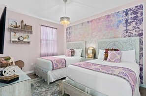 Un dormitorio con dos camas, una araña, detalles decorativos en la pared y una mesita de noche con lámpara.