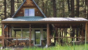 Une cabane rustique avec une façade en bois, une véranda couverte et une fenêtre donnant sur une zone boisée.