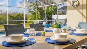 A sunlit dining area with a view of the outdoors, featuring a table set with white plates, bowls, and glasses, surrounded by chairs and potted plants. - Luxury 4 bed villa private pool & spa, close to Disney Parks on Golf Community (Davenport)