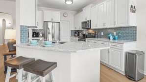 A modern kitchen with white cabinets, a stainless steel refrigerator, a microwave, and a sink. There is a clock on the wall and a trash can in the corner. - Luxury 4 bed villa private pool & spa, close to Disney Parks on Golf Community (Davenport)
