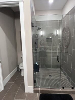 Moderni kylpyhuone, jossa on lasiseinällä varustettu suihku, laatoitetut seinät ja wc.