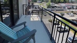 En balkon med et bord og stole, en blå bænk og udsigt til en parkeringsplads og bygninger.