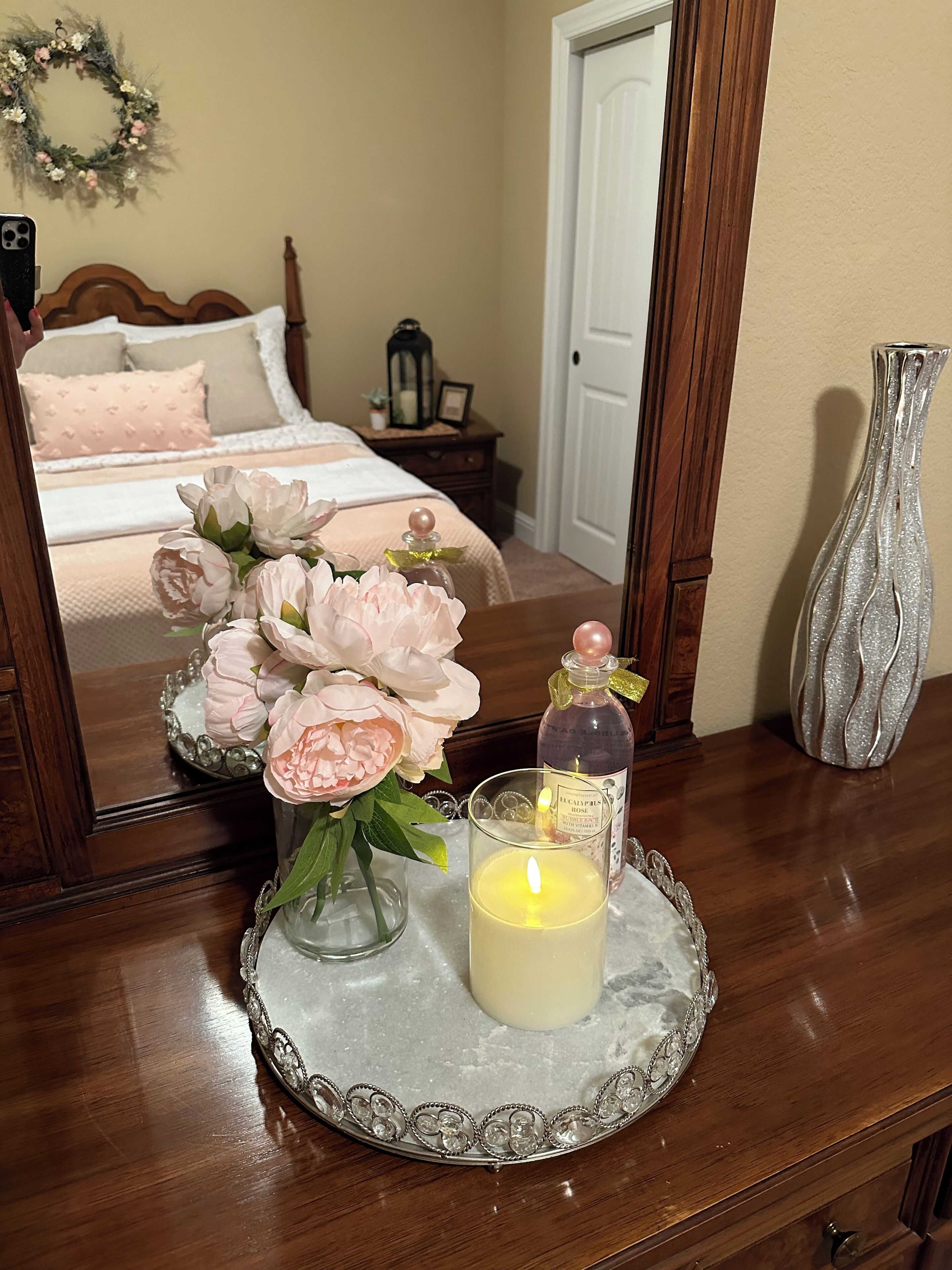 A bedroom with a wooden bed, a nightstand with a lantern, a vase with flowers, and a candle on a tray.