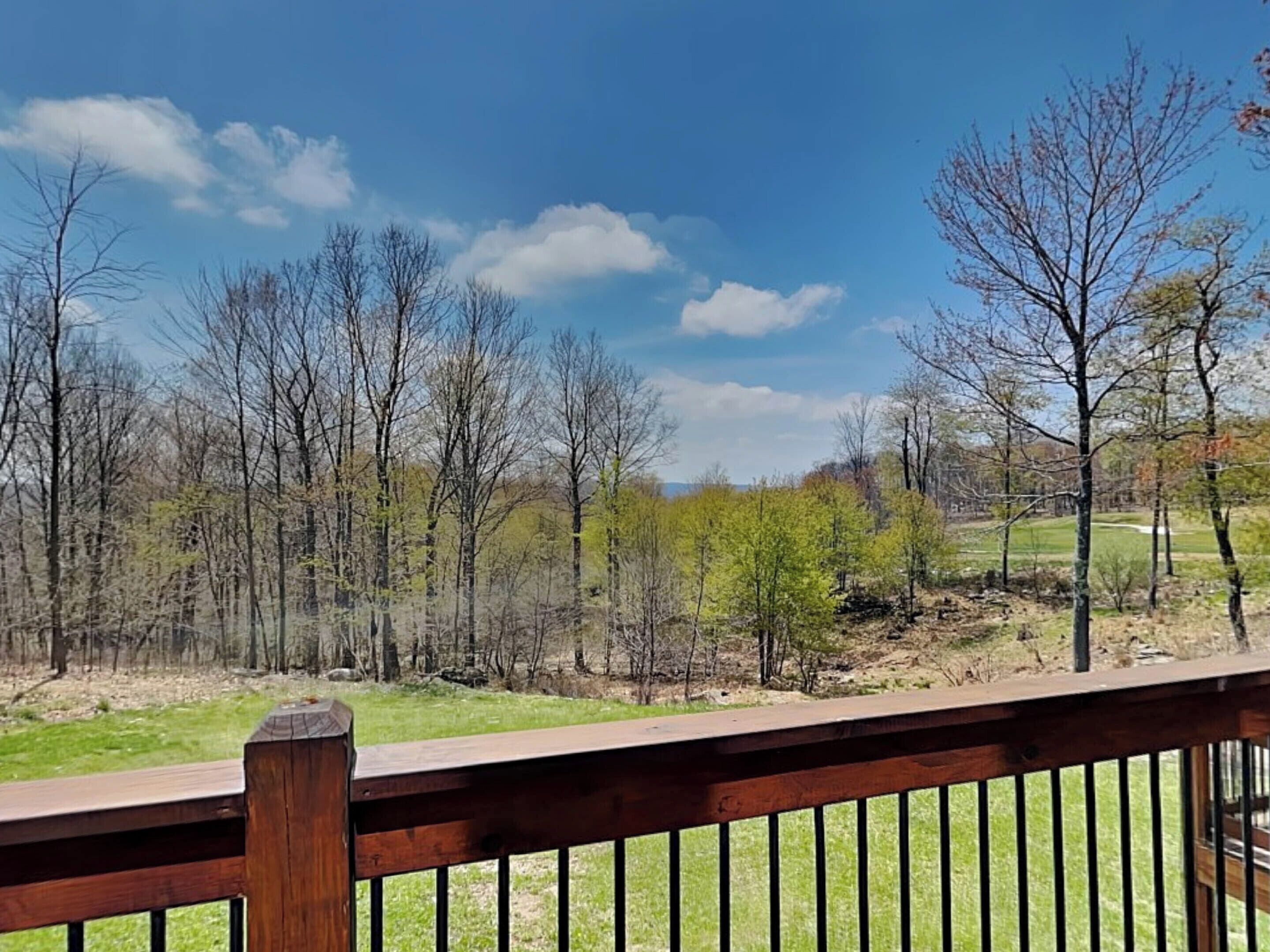 A wooden deck with a view of a forest and a grassy area.