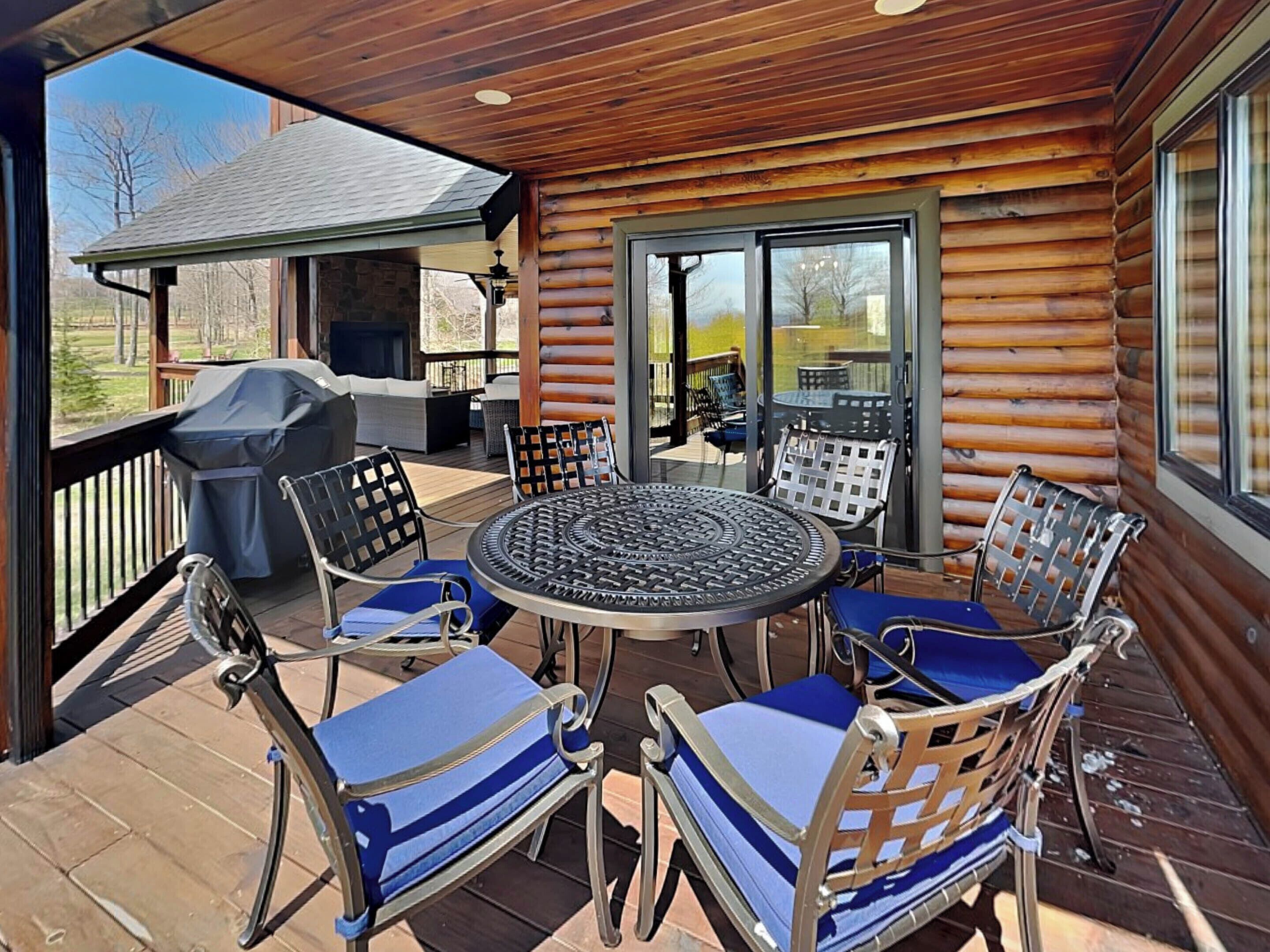 A covered patio with a round table and chairs, a grill, and a view of the outdoors.