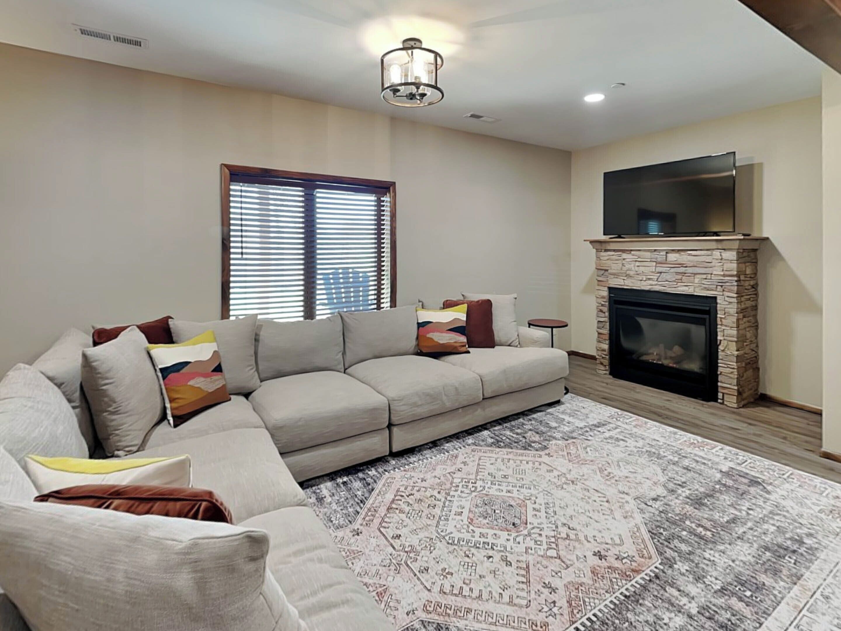 A living room with a sectional sofa, a fireplace, and a television mounted above it.