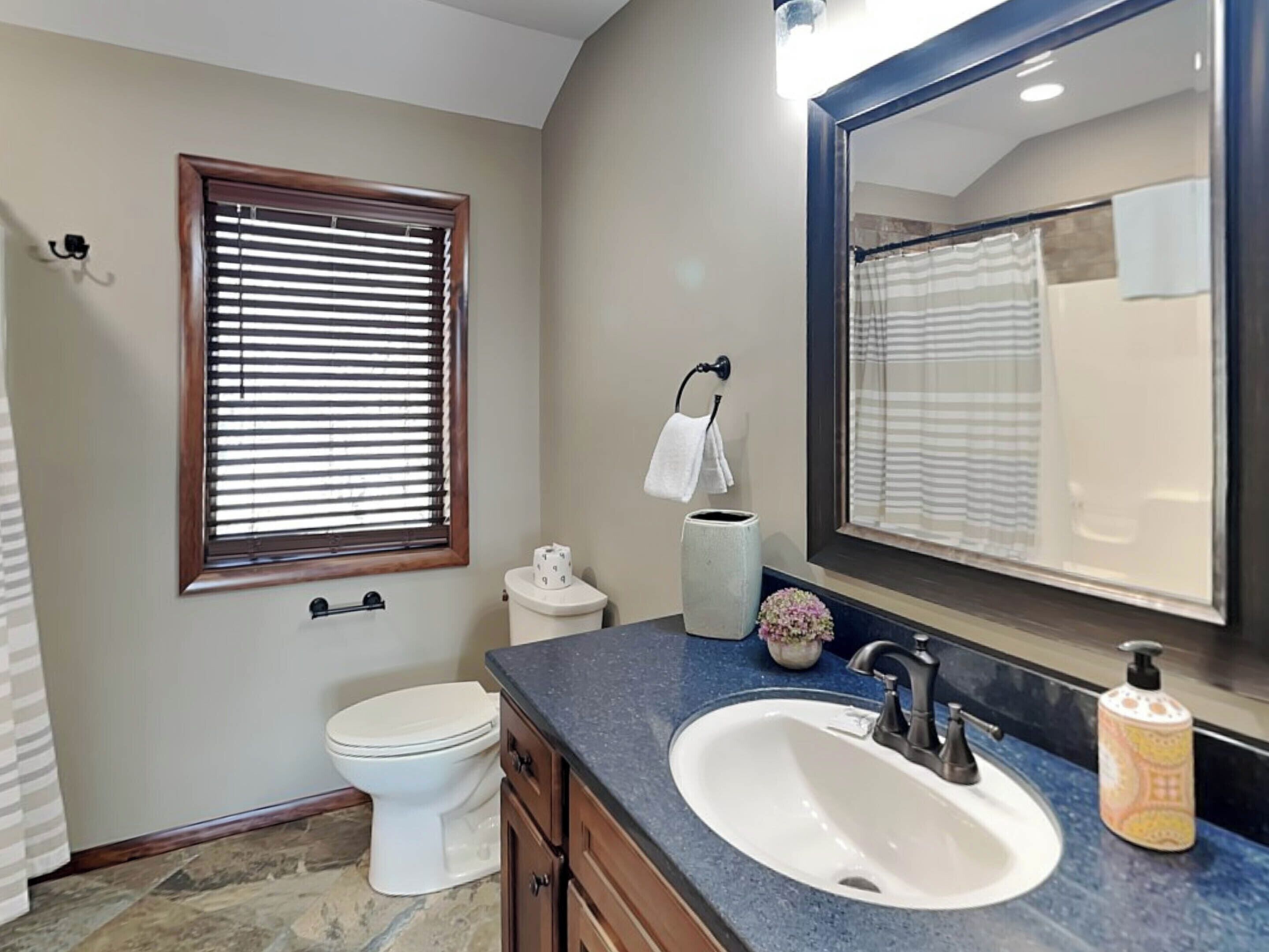 A bathroom with a toilet, sink, vanity, and a large mirror.