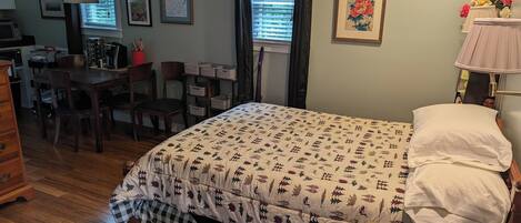 Un dormitorio con cama, escritorio, sillas, cómoda y ventana con cortinas.