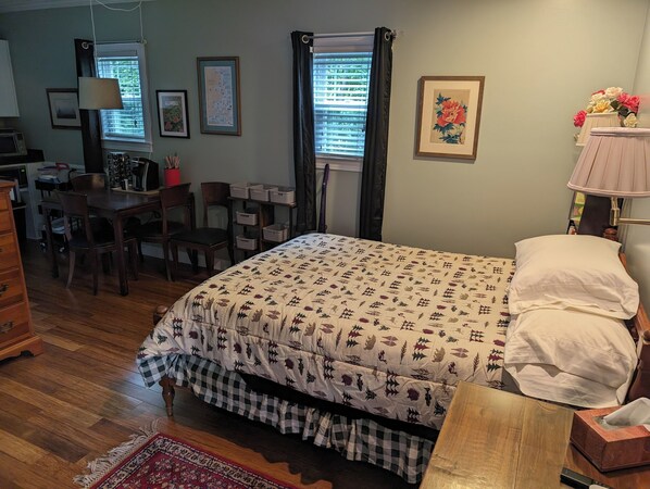 A bedroom with a bed, a desk, chairs, a dresser, and a window with curtains.