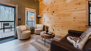 Una sala de estar acogedora con paredes de madera, un sofá, dos sillones, una mesita de centro y un balcón con una banca.