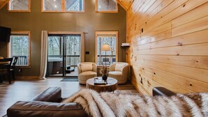 Interior acogedor de una cabaña con detalles de madera, una chimenea y un ventanal con vistas a una terraza.