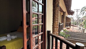 A room with a bed, a wooden door, and a balcony with a tiled floor and railing. - Pousada Sanhaço (Angra dos Reis)