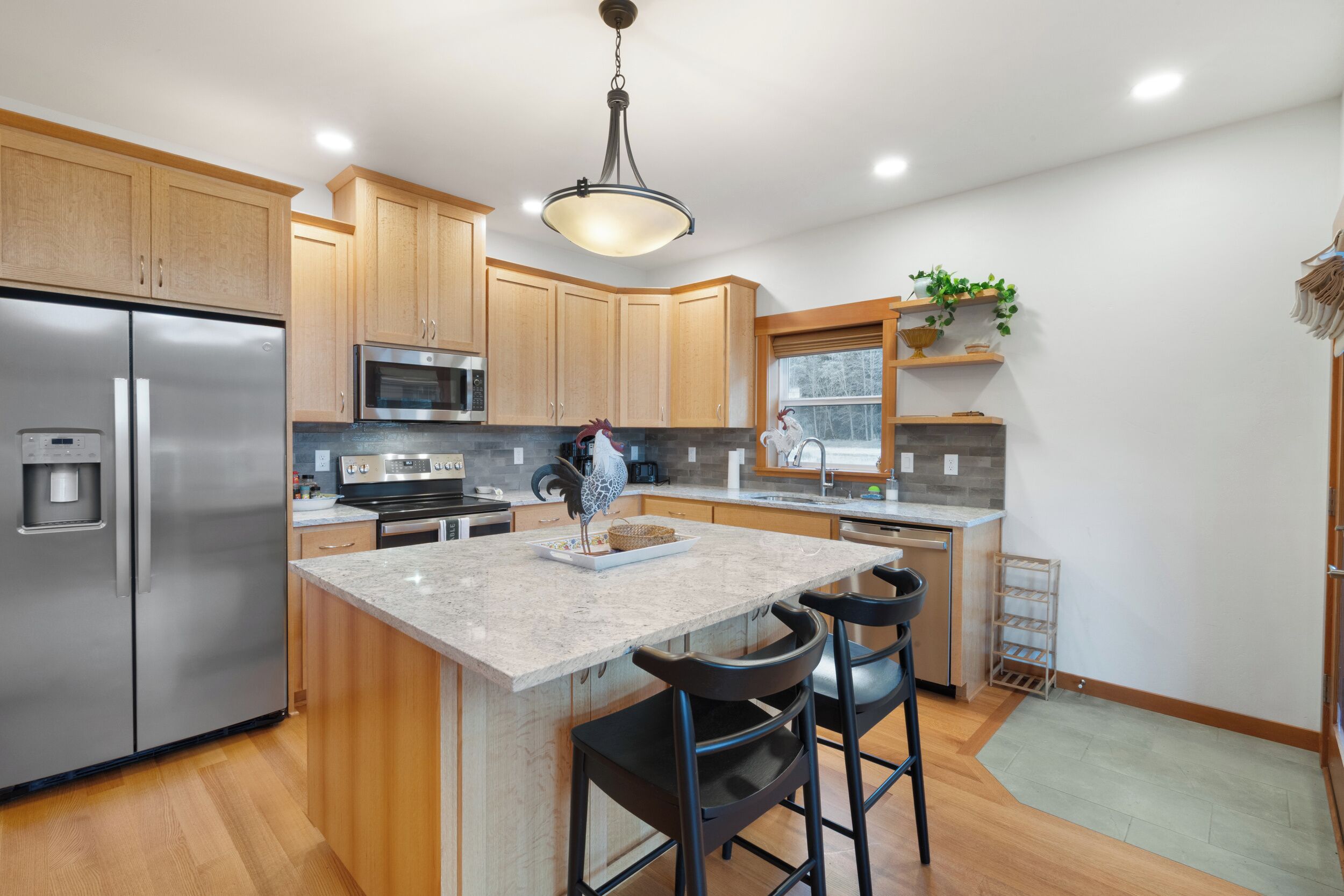 A modern kitchen with wooden cabinets, stainless steel appliances, a granite countertop, and a central island with bar stools.