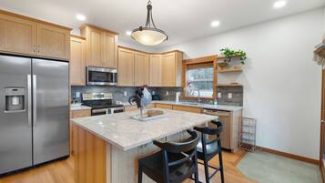 A modern kitchen with wooden cabinets, stainless steel appliances, a granite countertop, and a central island with bar stools.