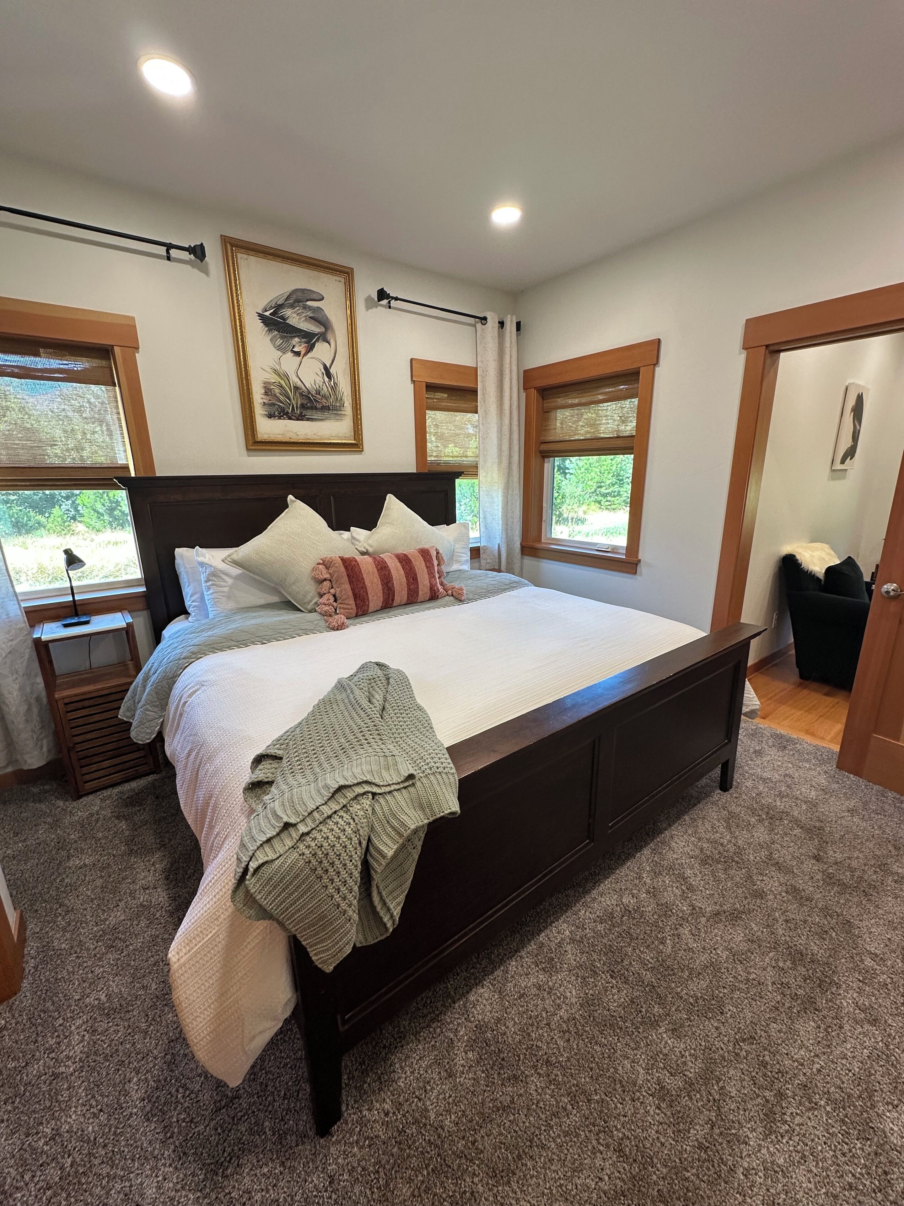 A bedroom with a large bed, a nightstand, a window with a view, and a door.