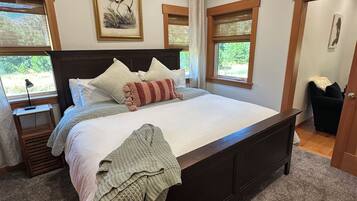 A bedroom with a large bed, a nightstand, a window with a view, and a door.
