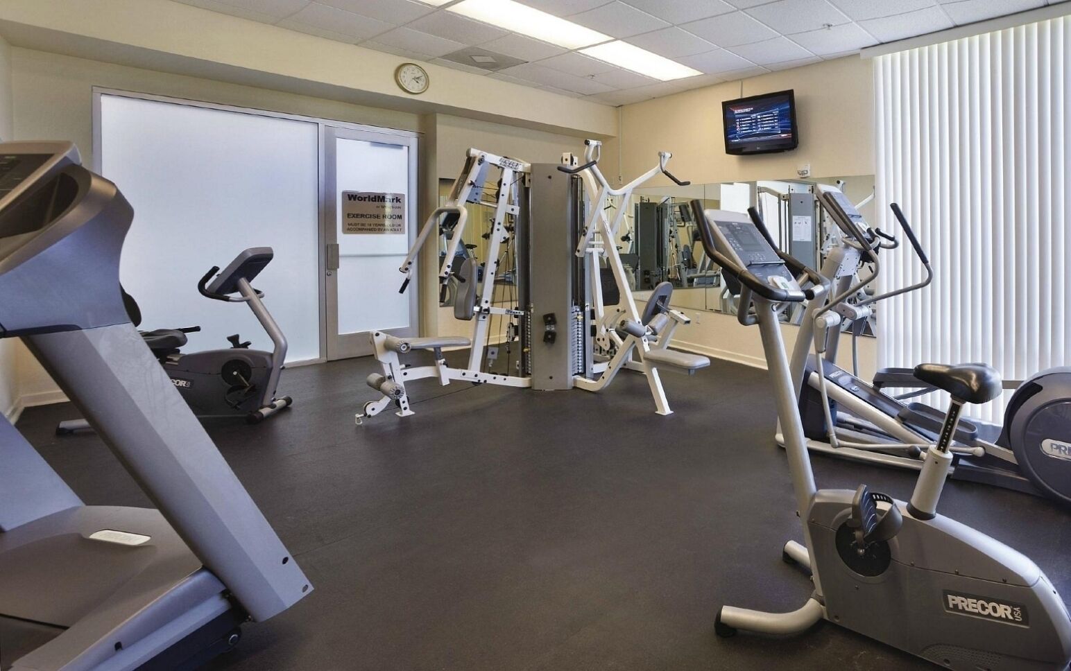 Un gimnasio con máquinas de cardio, equipo de entrenamiento con pesas y una pantalla de televisión.