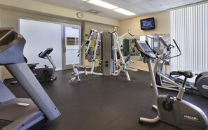 A gym with cardio machines, weight training equipment, and a television screen.