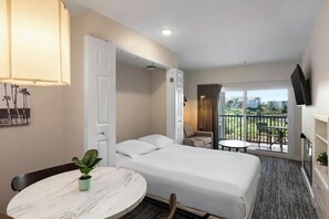 Ein Hotelzimmer mit einem Bett, einem runden Tisch mit einer Pflanze, einem Balkon mit Tisch und Stühlen sowie einem an der Wand befestigten Fernseher.
