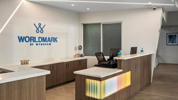 Bancada de recepção com um logotipo, dois monitores de computador, um telefone e uma pequena planta.