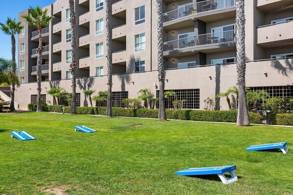 A multi-story hotel with balconies, a well-maintained lawn, and palm trees.