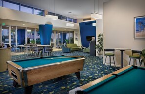 A pool table in a hotel lobby with a view of the outdoors through large windows.