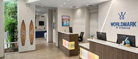 A reception area with a modern design, featuring a reception desk, a wall-mounted sign, and a painting.