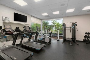 A gym with treadmills, elliptical machines, a weight bench, and dumbbells.