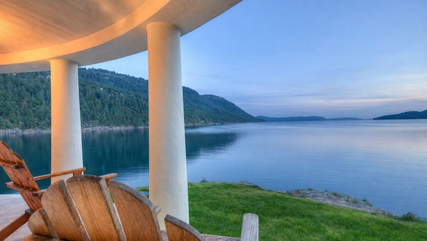 A lakeside view with a wooden deck and chairs, a covered area with columns, and a calm lake with distant hills. - Rosario Resort (Eastsound)