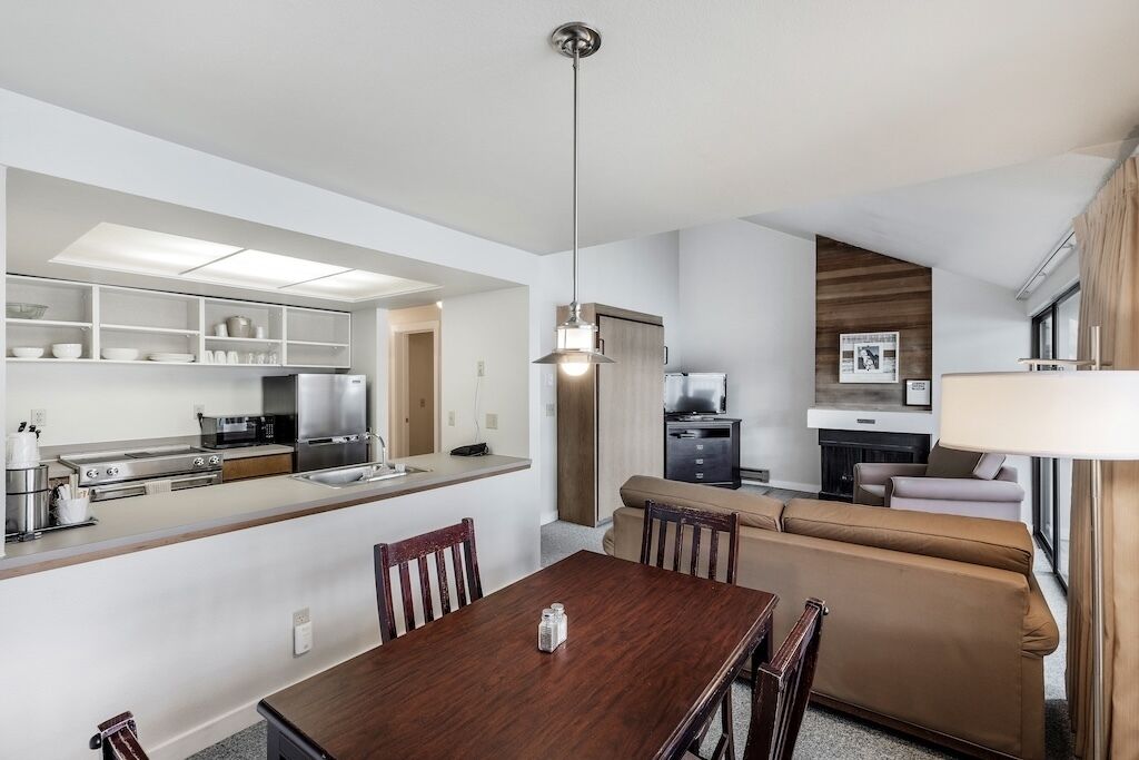 A modern kitchen with built-in appliances, a dining area with a wooden table, and a living area with a sofa and TV.