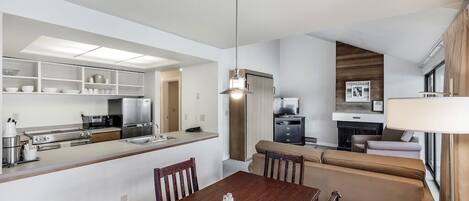 A modern kitchen with built-in appliances, a dining area with a wooden table, and a living area with a sofa and TV.