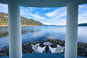 A gazebo with white columns and a table, overlooking a calm lake with a forested shoreline.