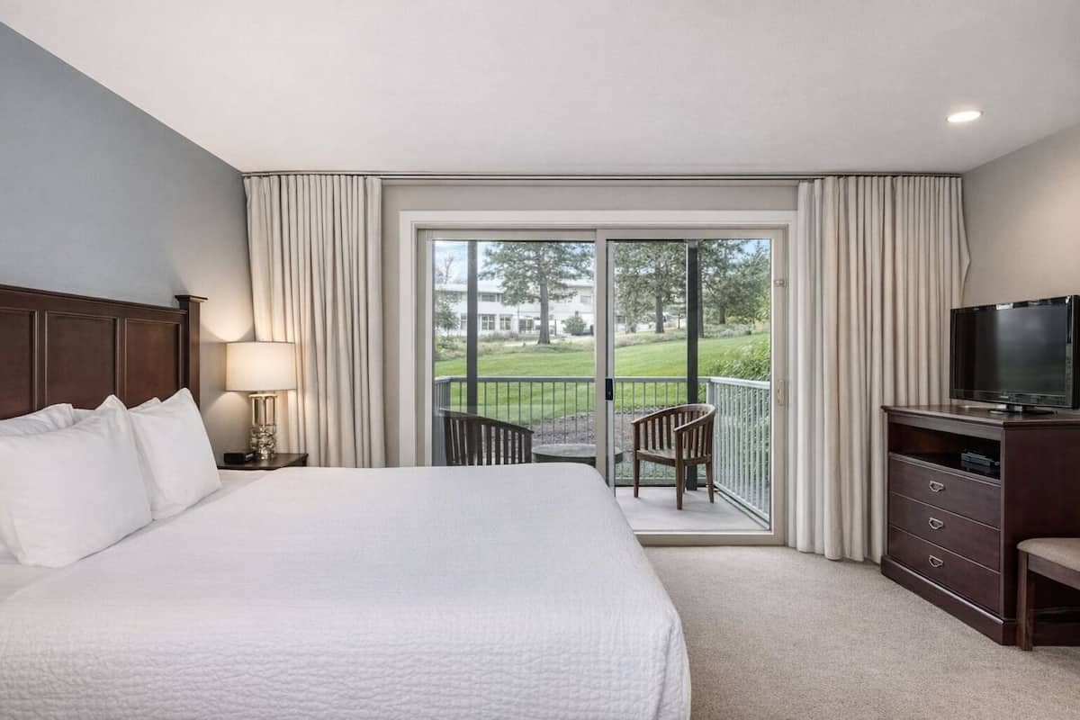 Een hotelkamer met een groot bed, een televisie, een bureau en een balkon met een stoel.