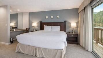 A large bed with a wooden headboard, two bedside tables with lamps, a desk with a chair, and a view of a balcony.