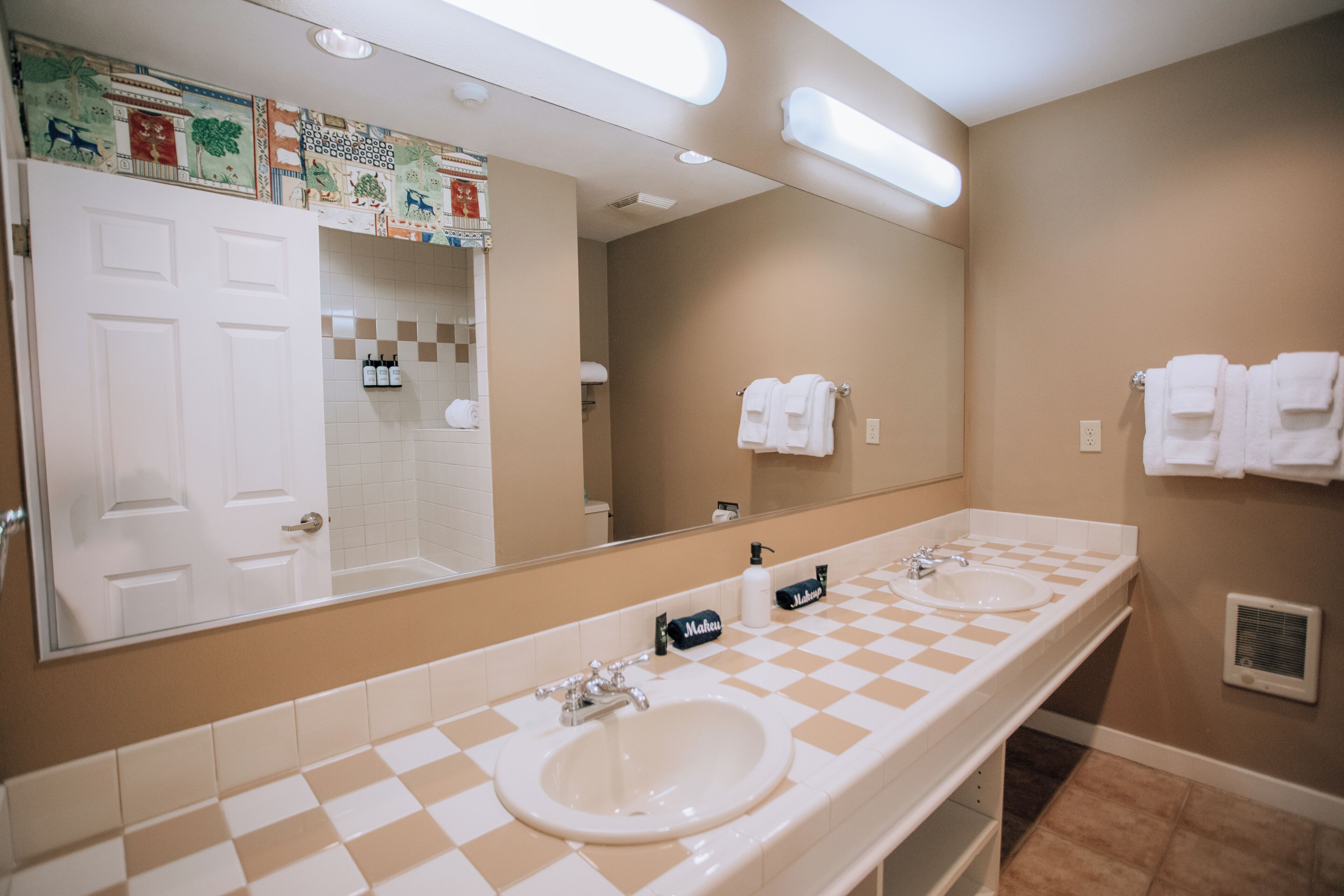 Un baño con dos lavamanos, un espejo grande y un salpicadero de azulejos a cuadros.