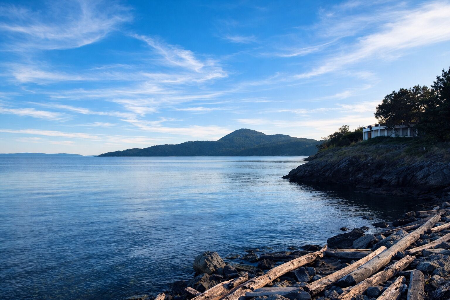 Un paisaje costero con agua tranquila, costa rocosa y montañas a lo lejos.