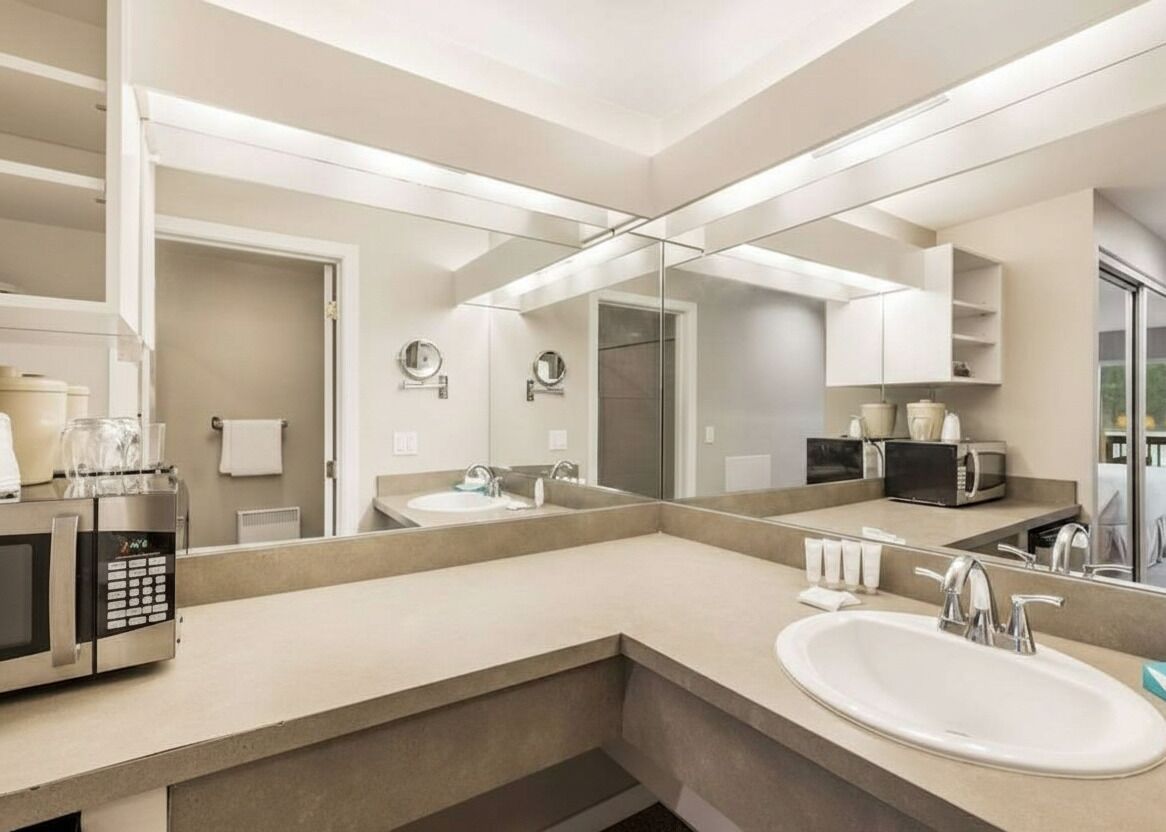 Un baño moderno con un espejo grande, un lavamanos, un microondas y una cafetera.