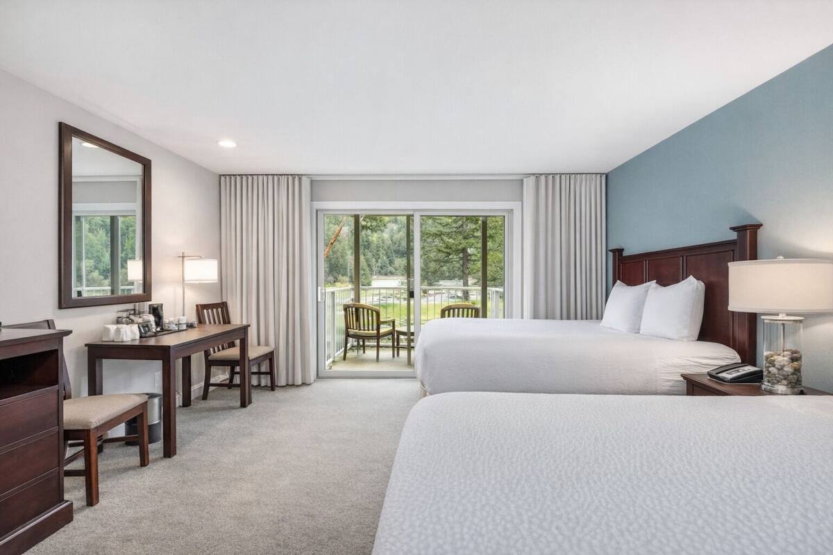Een hotelkamer met een bed, een bureau, een stoel, een lamp en uitzicht op een balkon met buitenmeubels.