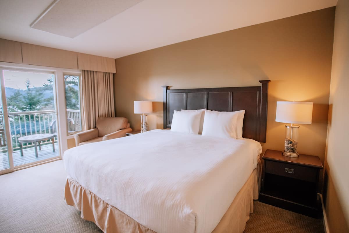Een hotelkamer met een groot bed, twee bedlampjes, een stoel en een balkon.
