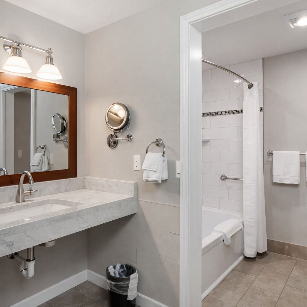 A modern bathroom with a marble sink, two wall-mounted mirrors, a handheld showerhead, and a bathtub with a shower curtain.