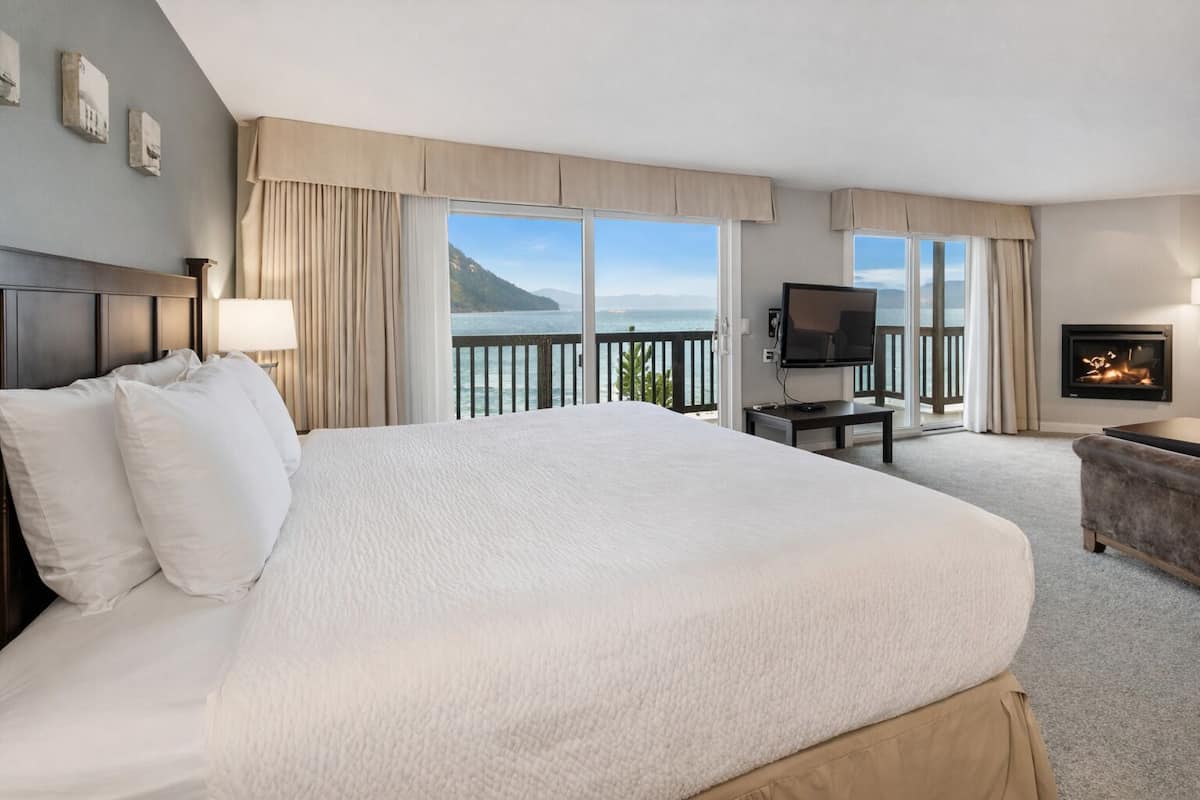 Een hotelkamer met een groot bed, een televisie, een open haard en een balkon met uitzicht op zee.