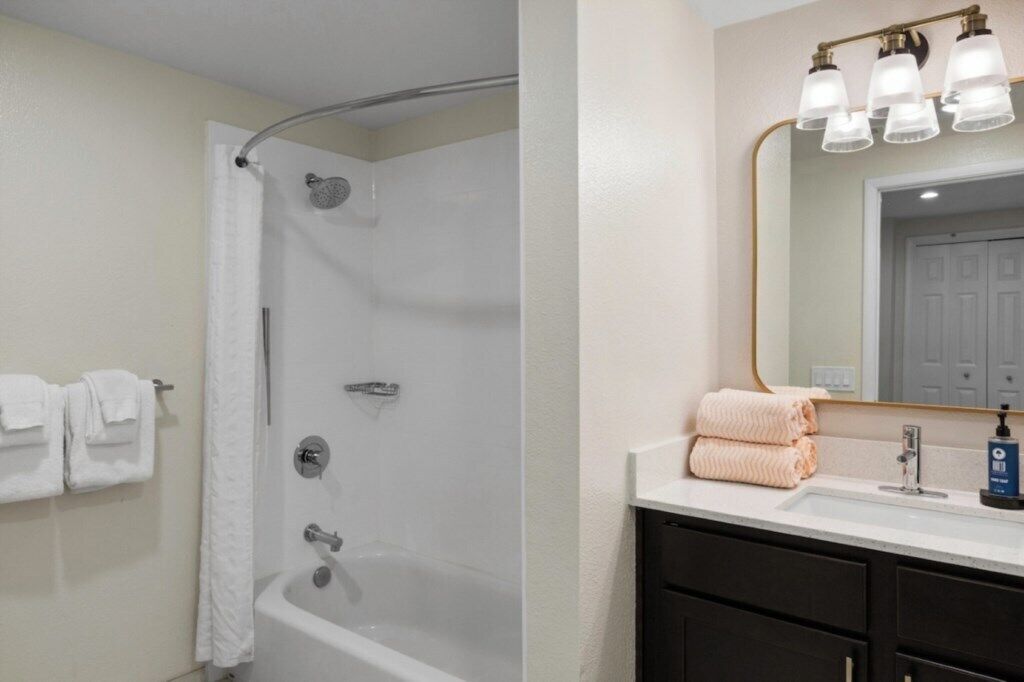 Un baño con ducha, un lavabo con espejo y toallas colgadas en la pared.