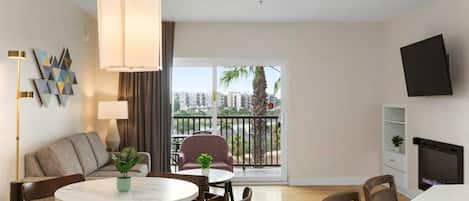 Una sala de estar moderna con una mesa de comedor redonda, sillas, un sofá, un televisor y un balcón con vistas a edificios y palmeras.