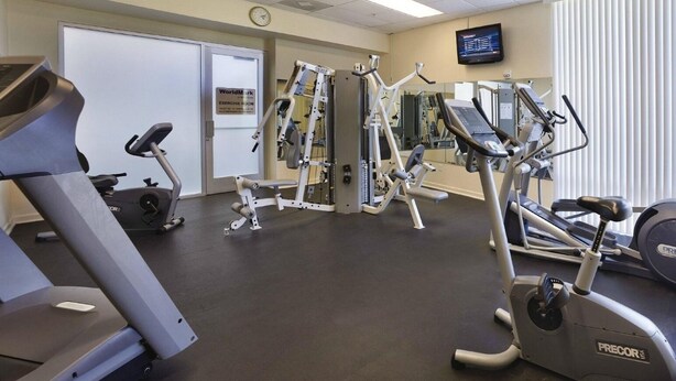 Et fitnesscenter med løbebånd, styrketræningsudstyr og en tv-skærm.