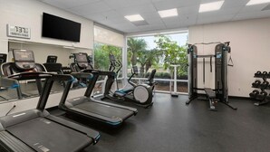 Un gimnasio con cintas de correr, elípticas, una banca de pesas y mancuernas.