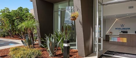 A modern building with a reception desk, a glass entrance, and a landscaped area with plants.
