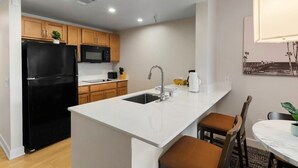 Una cocina moderna con un refrigerador negro, armarios de madera, una encimera blanca y un comedor con una mesa redonda y sillas.