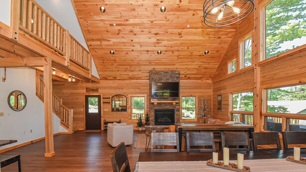 A spacious wooden cabin interior with a fireplace, dining area, and large windows offering views of the outdoors. - Luna Stella Lodge-6BR Mt View, Hot Tub, Fire Pit (McHenry)